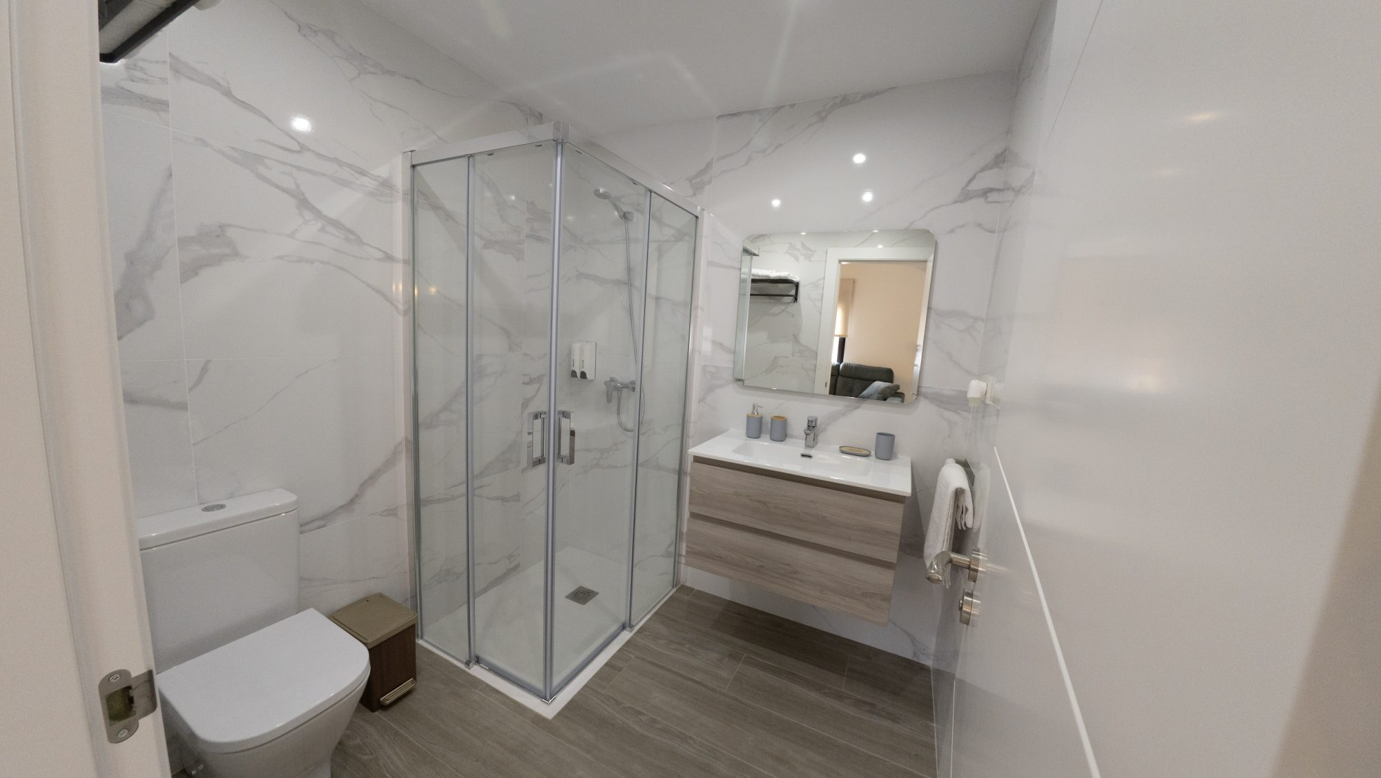 Baño revestido en mármol Calacatta con ducha de cristal y mueble de madera clara.