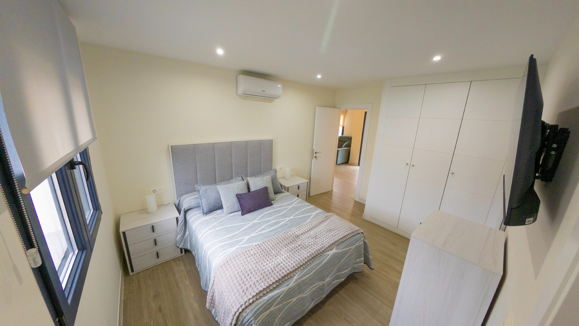 Dormitorio principal con cama de matrimonio, cabecero gris acolchado y armario empotrado blanco.