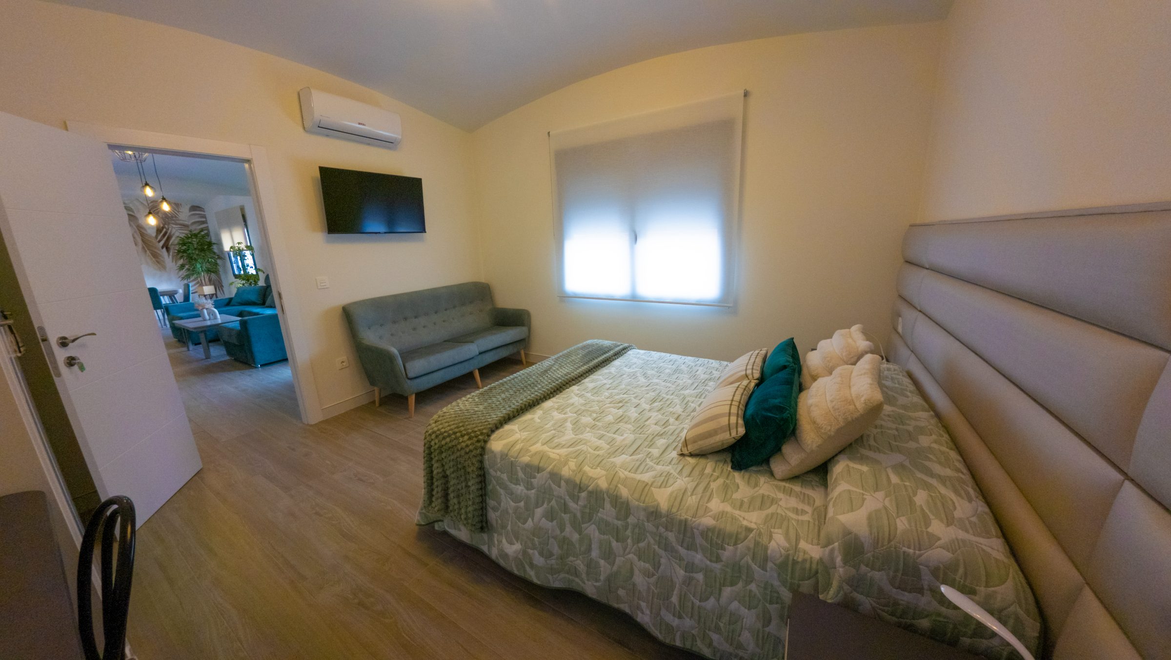 Dormitorio con cama doble vestida en tonos verdes y sofá auxiliar tapizado en azul.